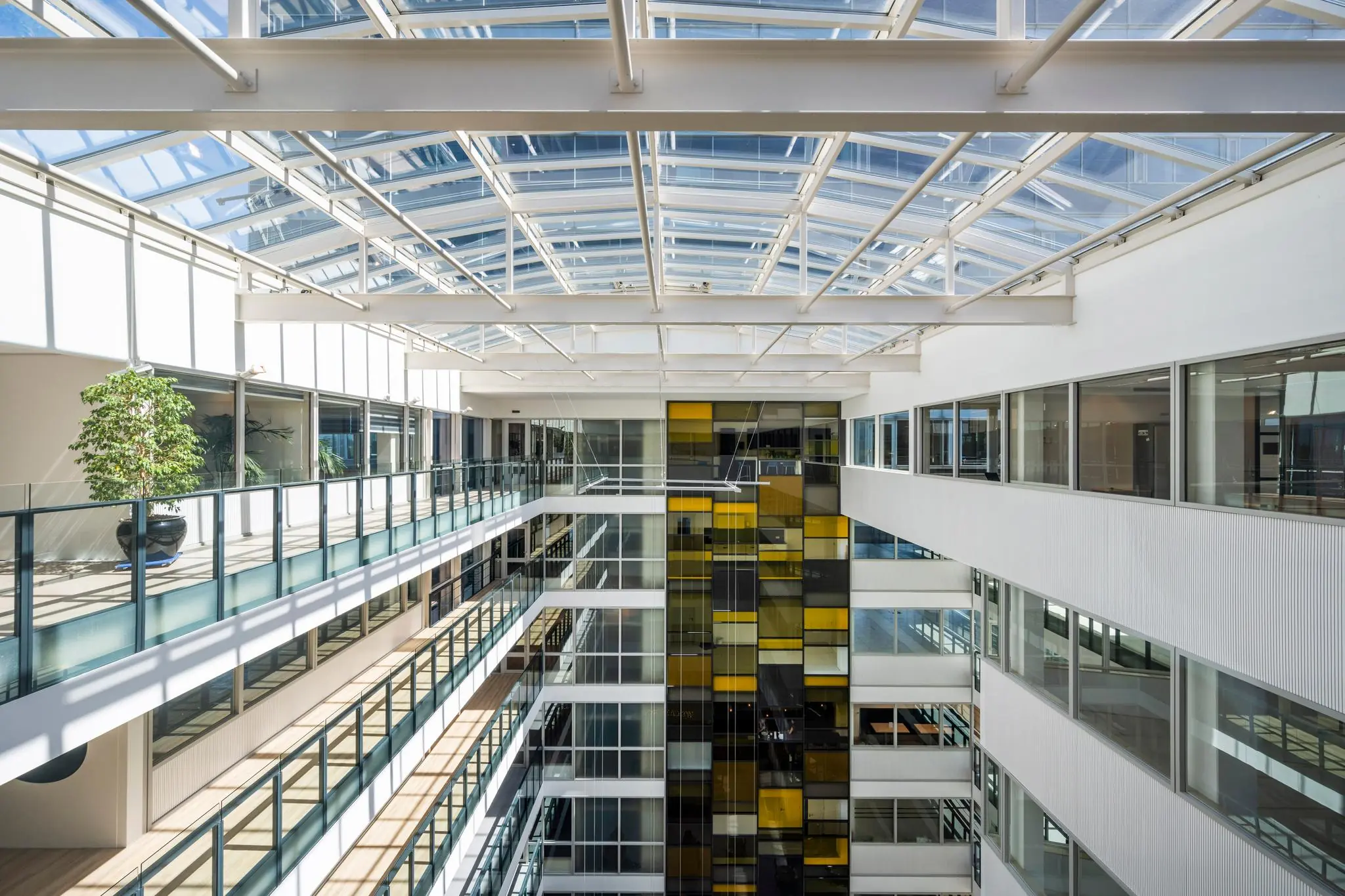 Licht atrium van een modern kantoorgebouw aan de Thomas R. Malthusstraat met glazen dak en kleurrijke gevelpanelen.